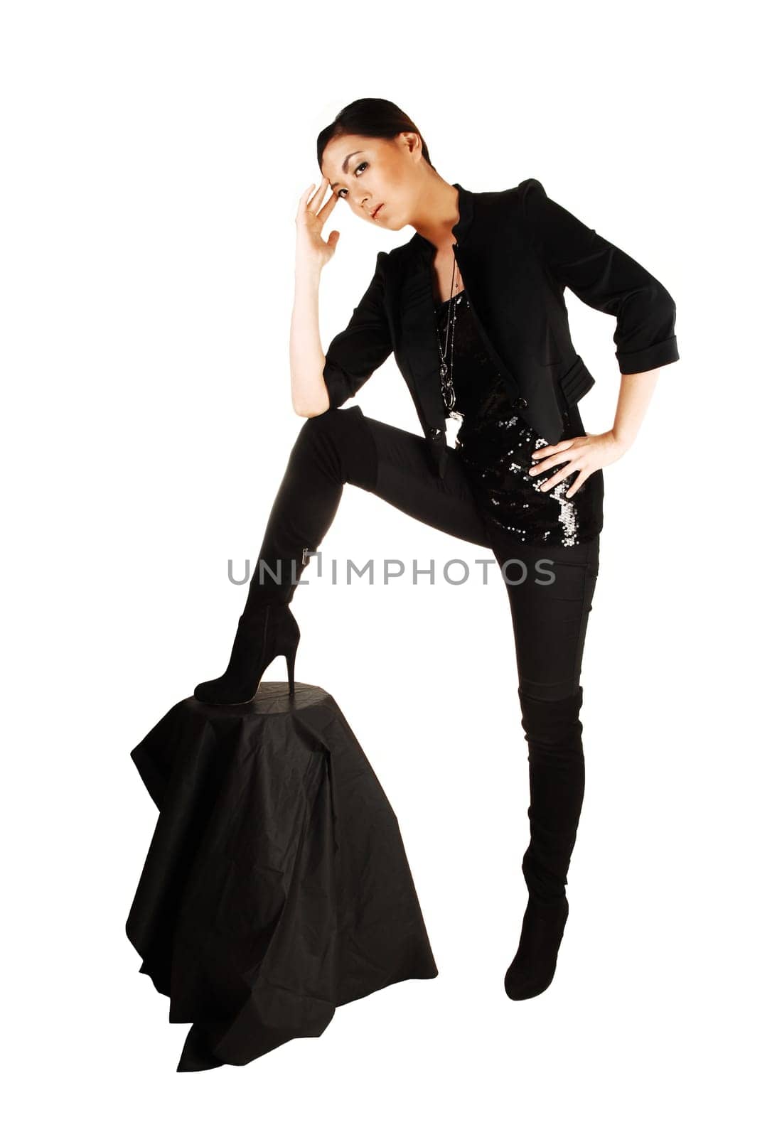 A tall young and slim chinese woman standing with one leg on a chair for white background in black tights and long black boots for white background.