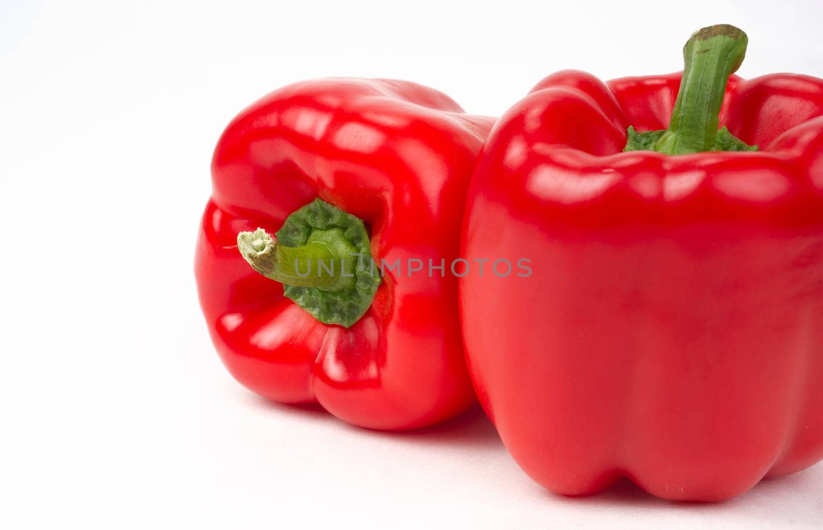Bright Red Vegetable Peppers Sit in a Pair on a WHite Background