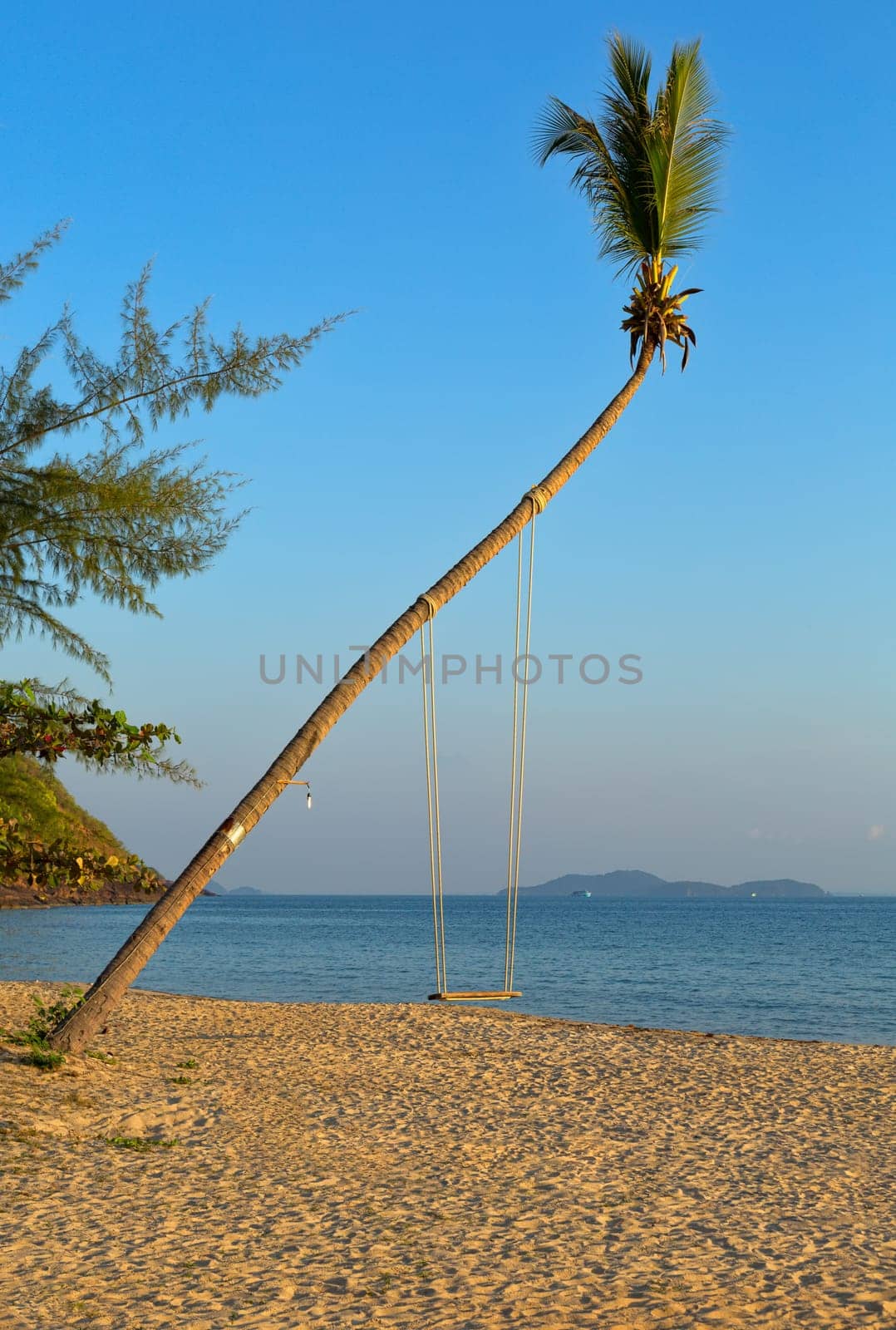 Empty swing hanging from a tree on romantic Thai beach at sunset