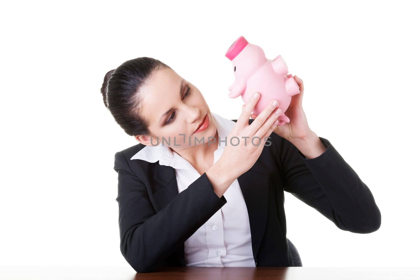 Happy business woman with her savings in piggy bank at the desk, isolated