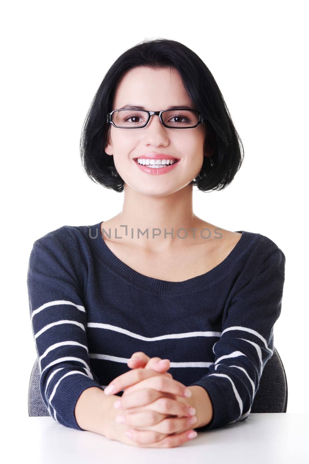 Pretty, happy, young woman in casual clothes sitting at the desk, isolated on white