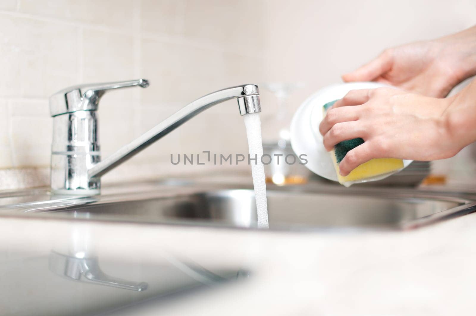 woman hand holding yellow sponge and washing saucer with washed dishes in background