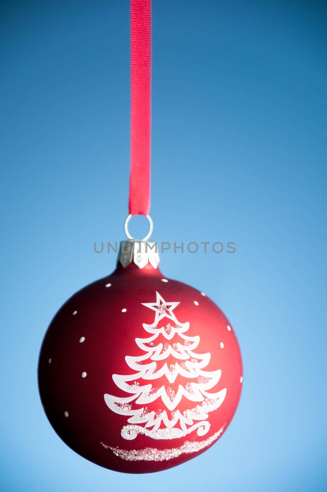 red christmas toy ball hanging on the red ribbon against blue background