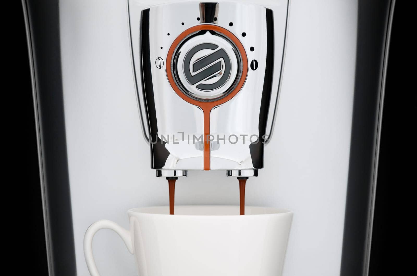 close up front view of modern automatic espresso coffee machine. White cup under nozzle, coffee pouring down from machine, black background