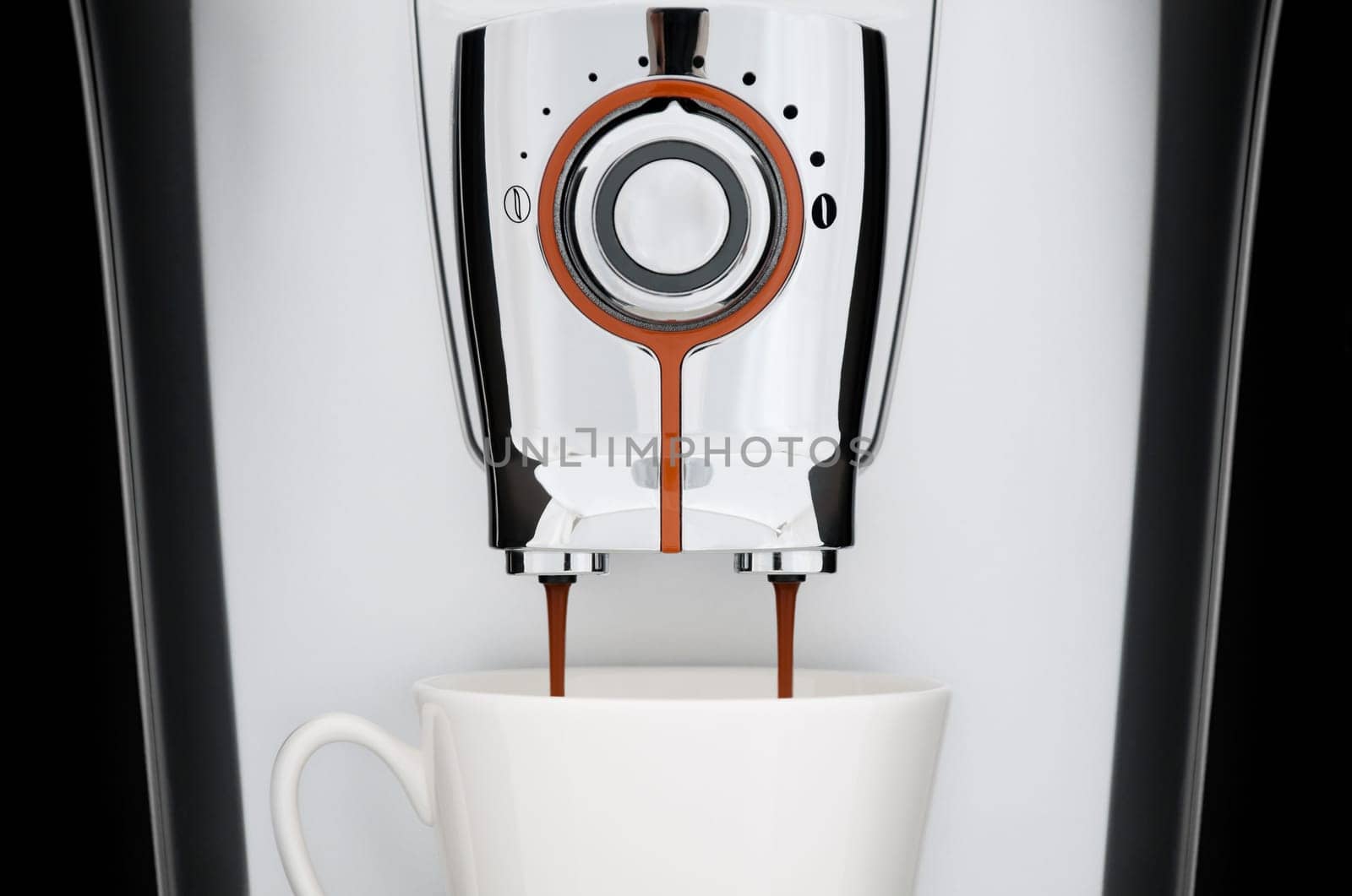 close up front view of modern automatic espresso coffee machine. White cup under nozzle, coffee pouring down from machine, black background