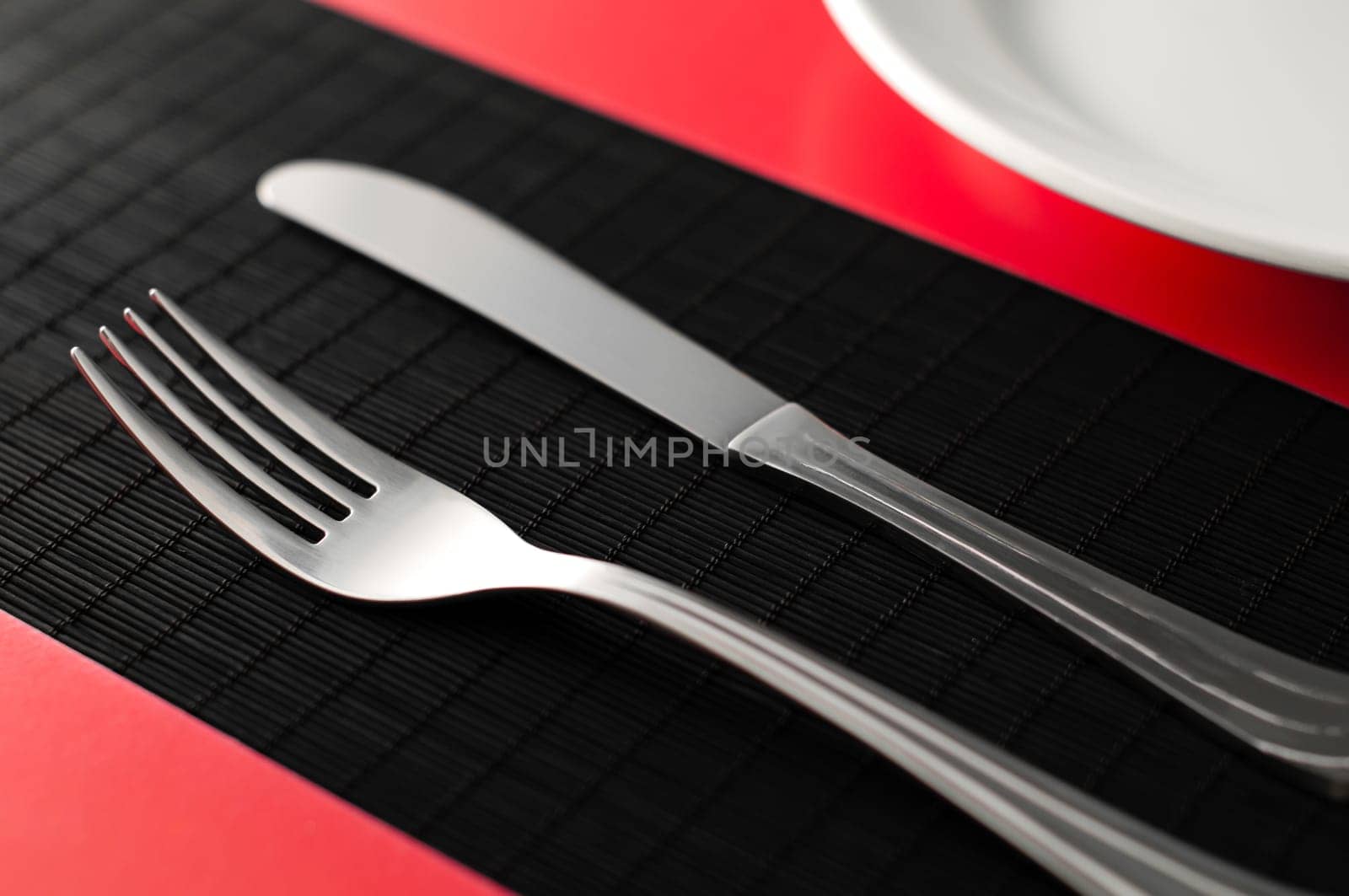 empty white plate on red napkin with knife and fork on black table at the side of the plate