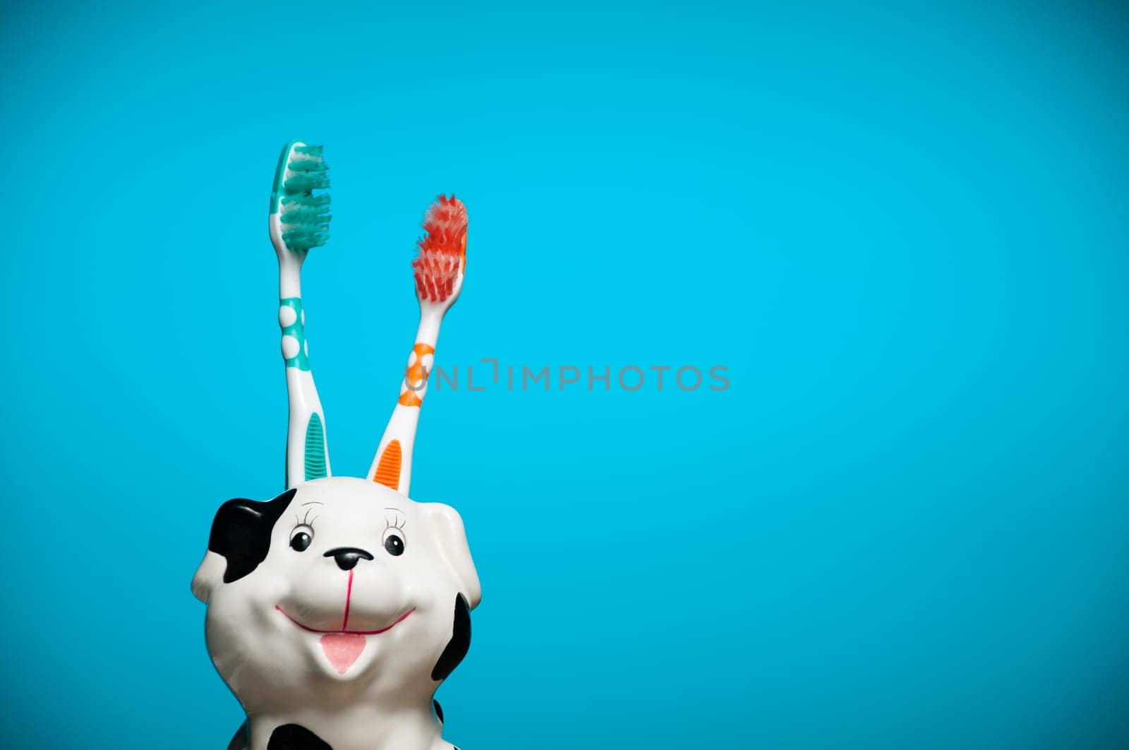 two toothbrushes in the glass resembling smiling dalmatian dog's head against blue background