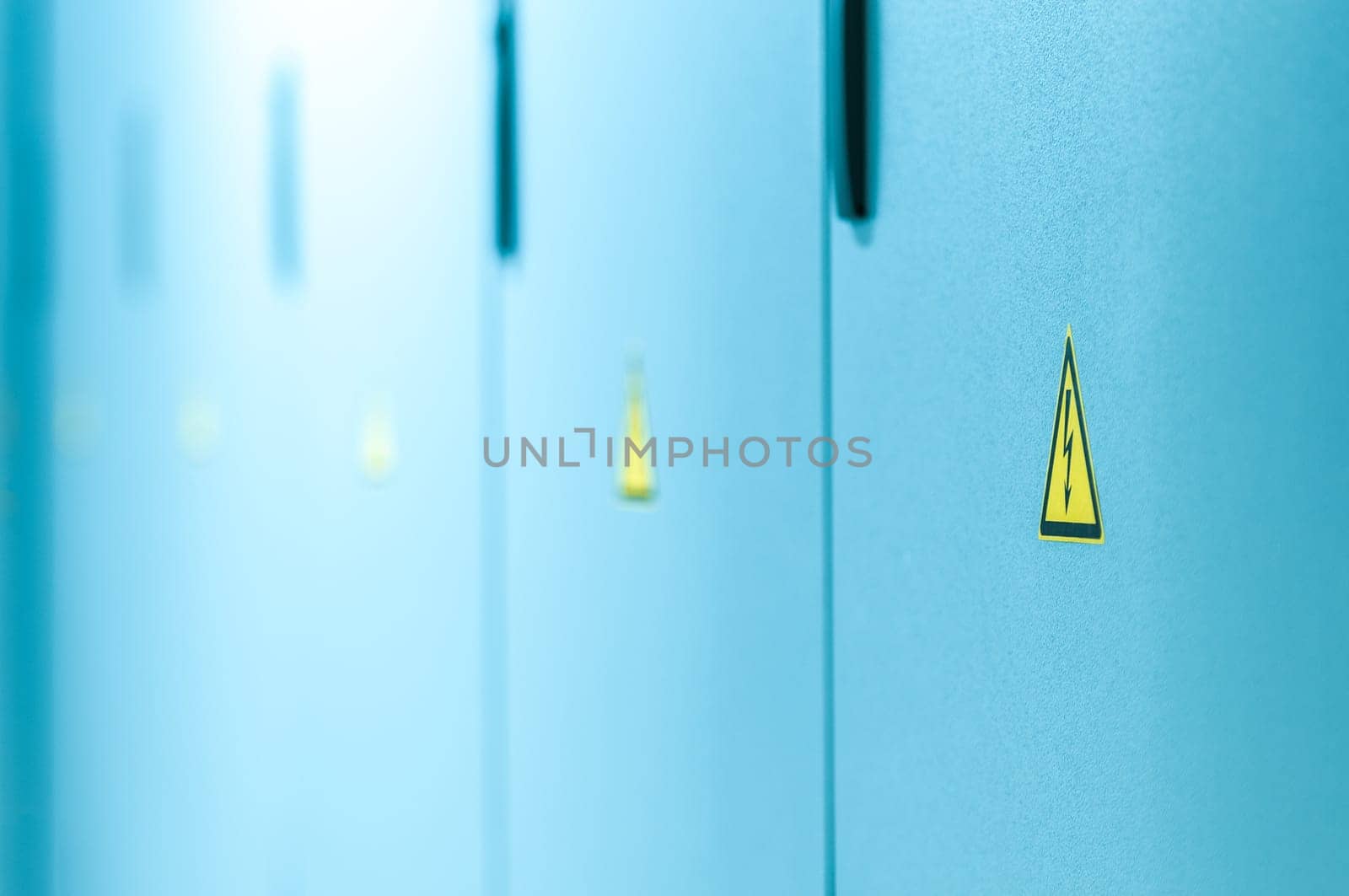 Blue closed doors with high voltage sign on it. Black and yellow triangle with flash. International safety symbol. Vanishing line of multiple doors. Equipment in server with electricity hazard signs.