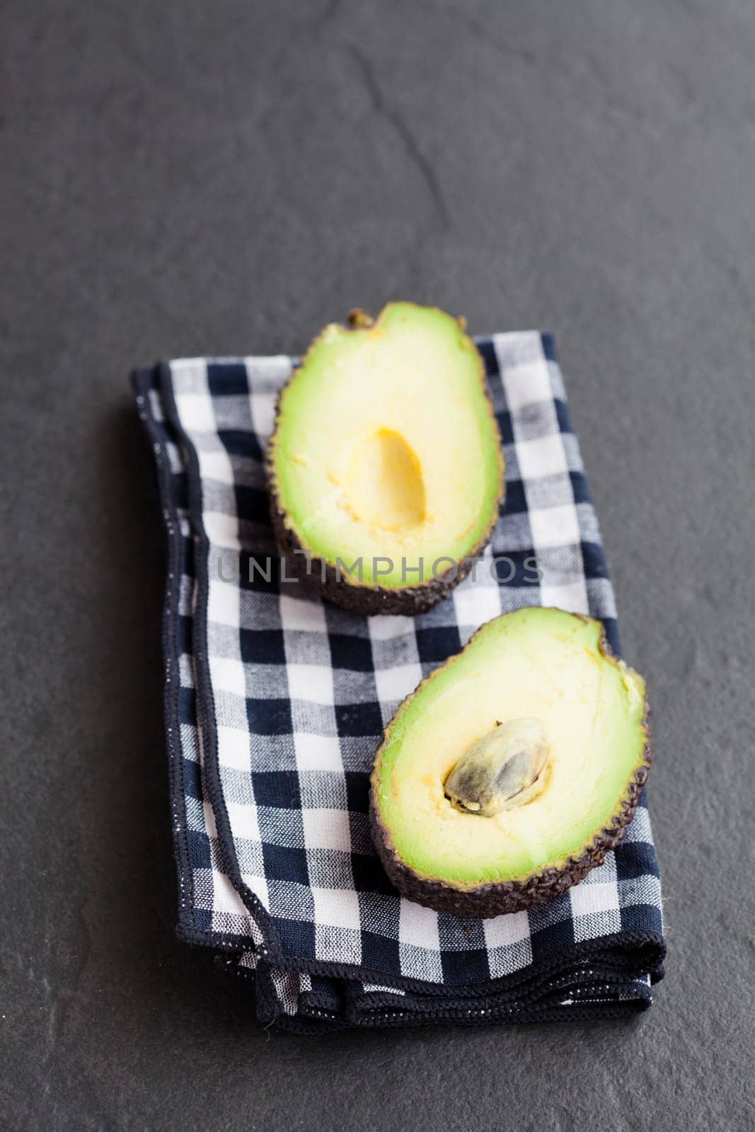 Closeup of fresh avocado halves resting on checkered napkin on dark background