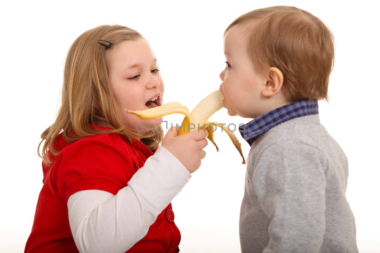 The photo shows a pair of siblings,with the girl feeding her brother a banana.
