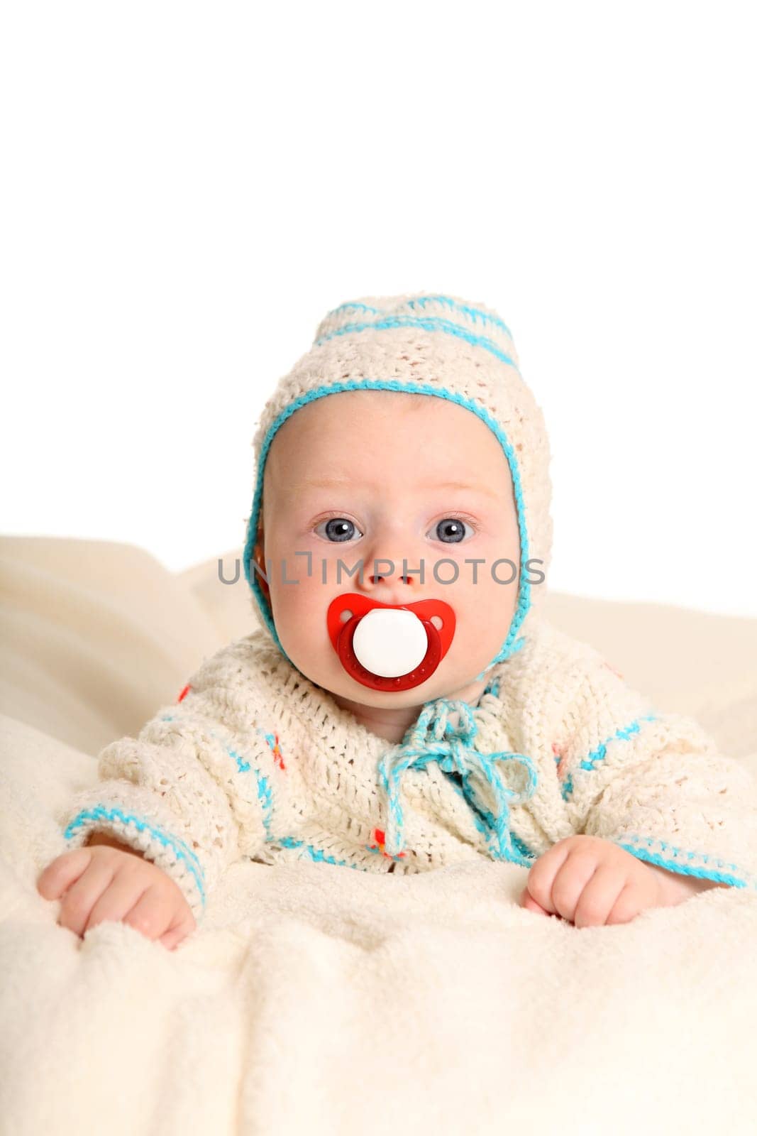 A small baby lies on his stomach with a pacifier and looks into the camera with wide eyes.