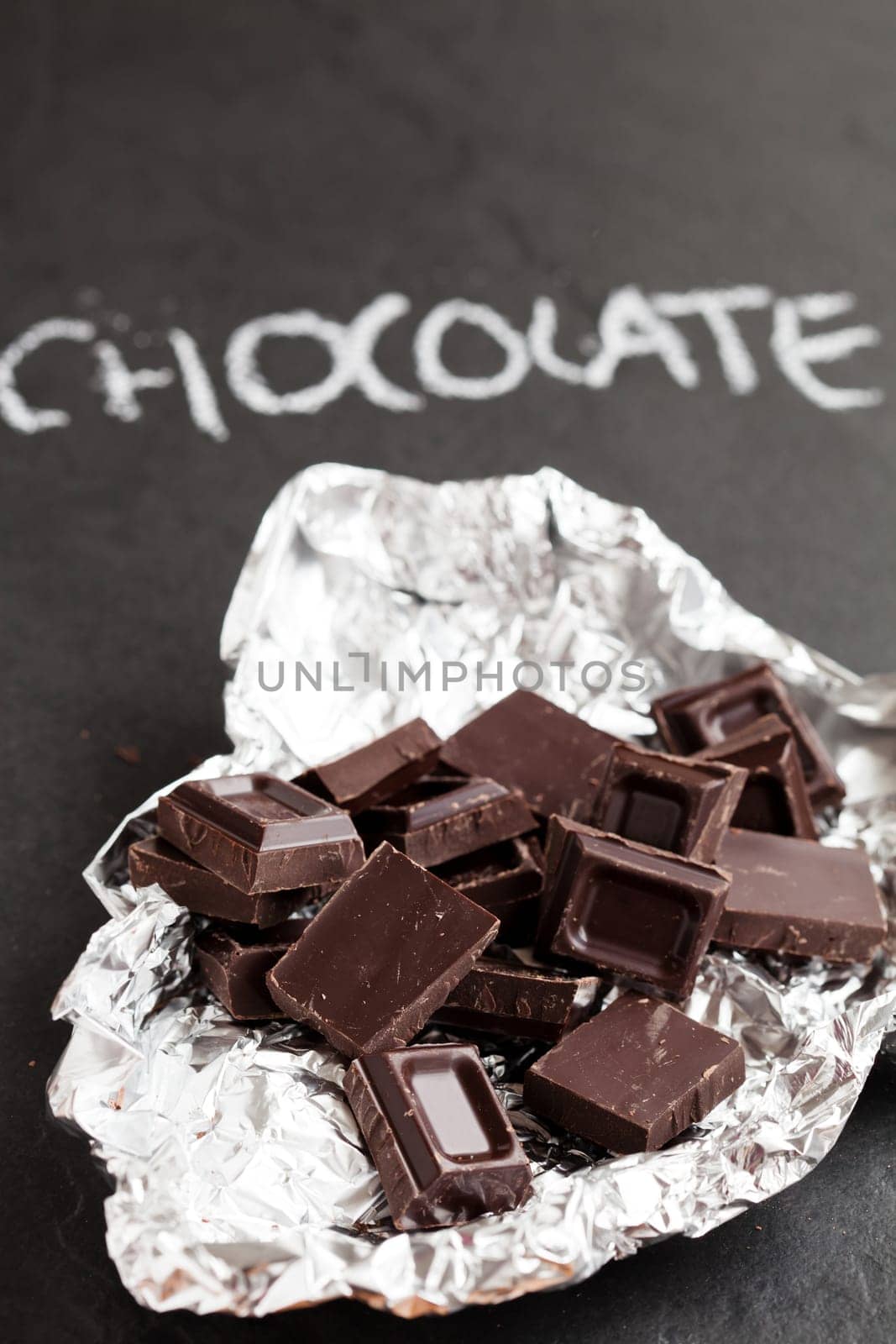 Closeup of chocolate squares in silver foil with word chocolate written in chalk on dark background
