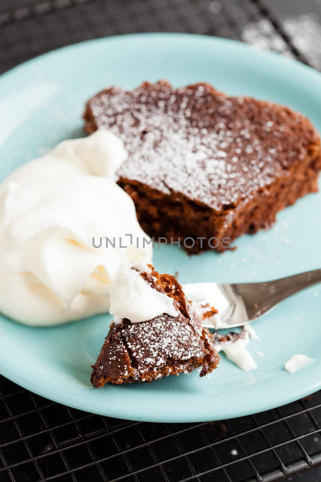 Closeup of slice of chocolate cake and whipped cream on plate resting on mesh metal tray