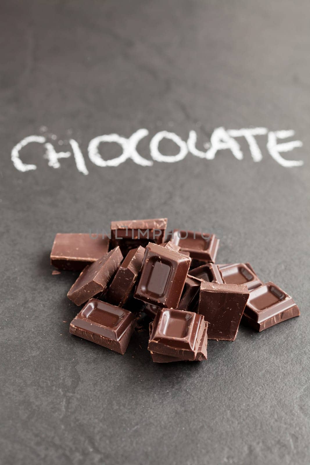 Closeup of pile of chocolate squares with word chocolate written in chalk on dark background