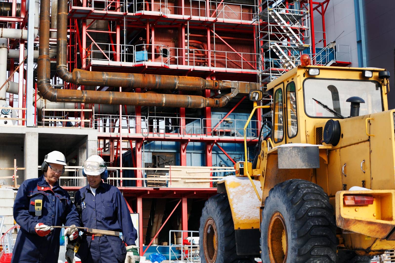 two site workers in hard-hats inside large construction industrial site.