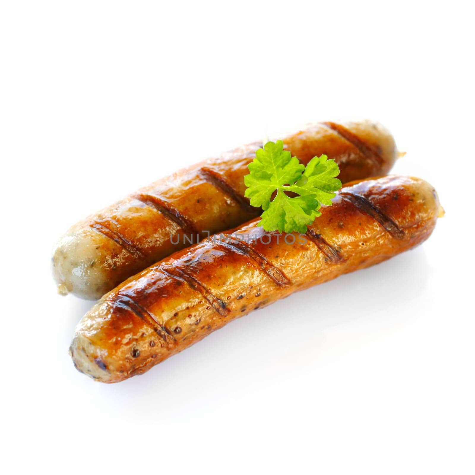 Close up of two cooked sausages, focus on the one at the front with a sprig of parsley on top against white background.