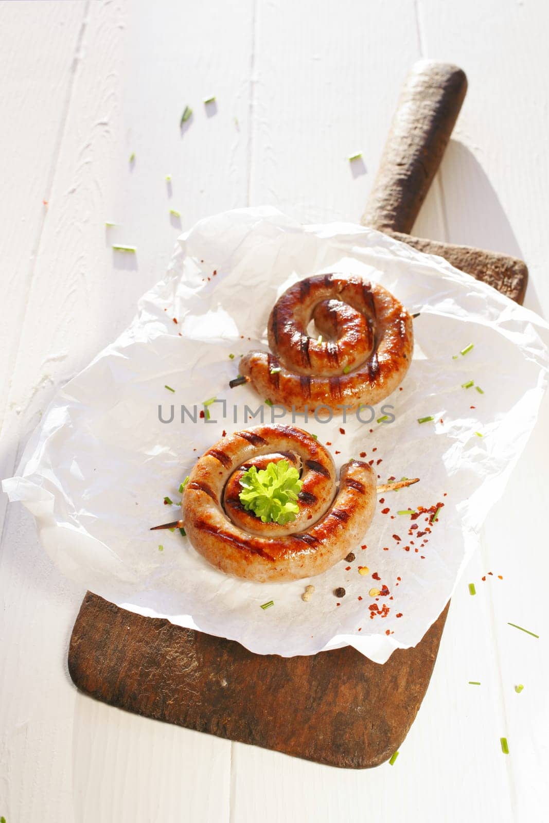 Two cooked sausages in a swirl shape on a wooden platter on a white table.