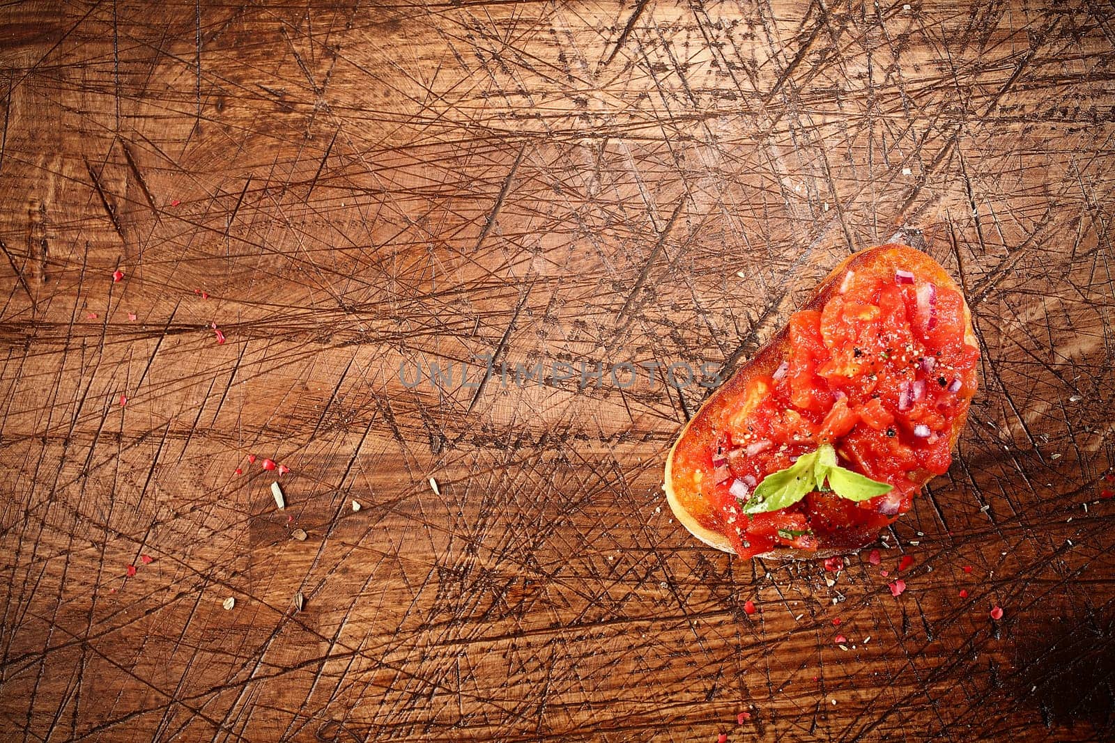Overhead view of colourful red tomato bruschetta on toasted or grilled baguette lying on an old grunge badly scored wooden chopping board with copyspace