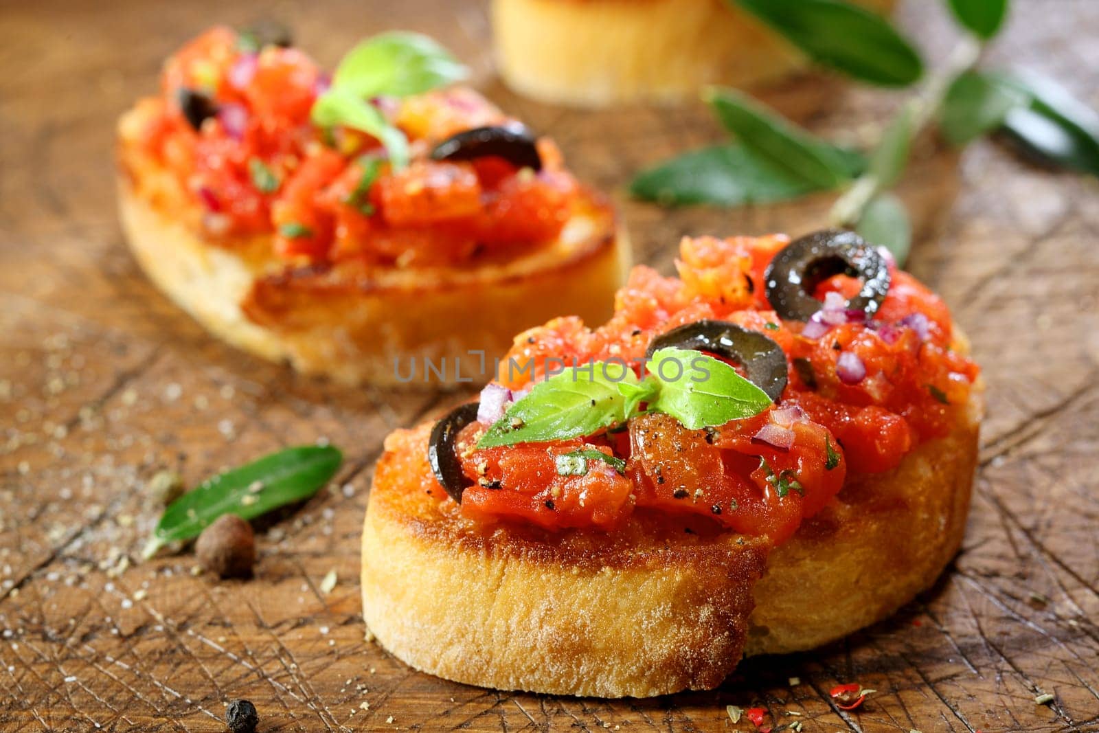 Preparing delicious Italian tomato bruschetta with chopped vegetables, herbs and oil on grilled or toasted crusty baguette sprinkled with seasoning and spices on an old grungy wooden chopping board