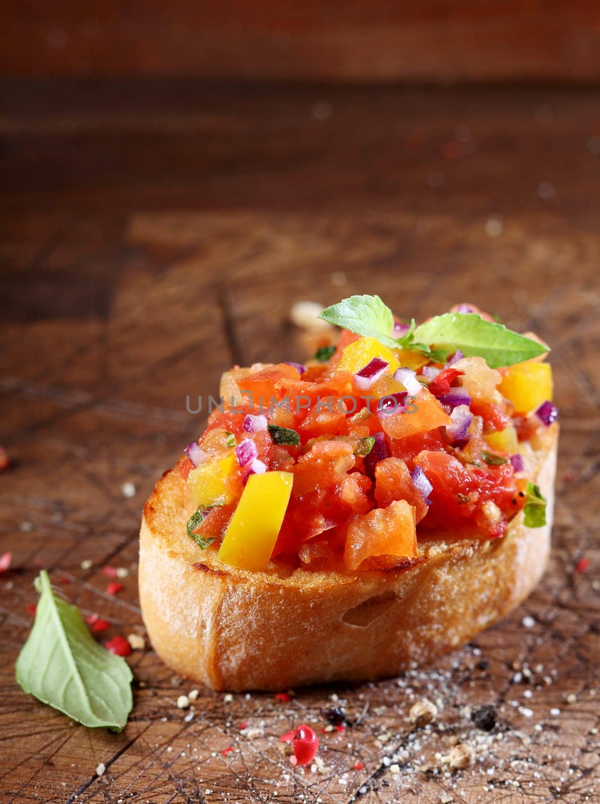 Tomato bruschetta or antipasti with a finely chopeed tomato and onion mixed with oil on a slice of crisp crusty toasted baguette surrounded by a scattering of spices on a wooden surface with copyspace