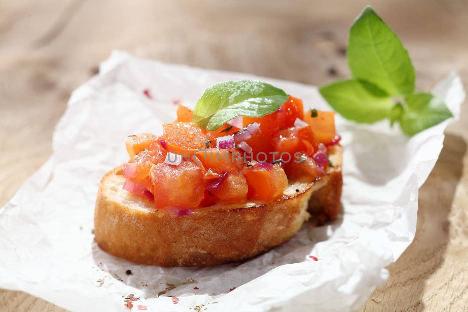 A single colourful tomato bruschetta Italian antispasti on crisp crusty toasted baguette on a sheet of crumpled white paper