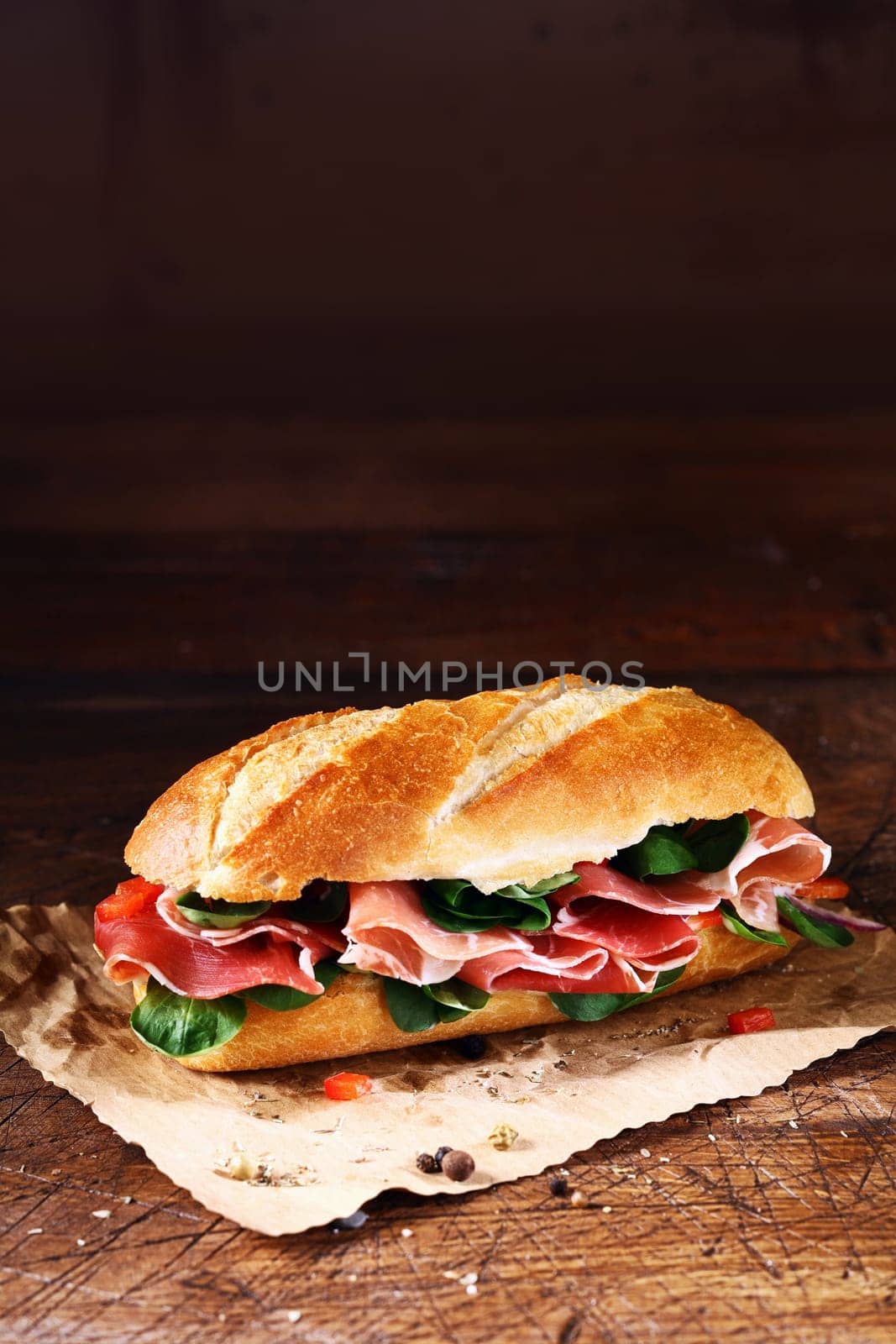Fresh basil and thinly sliced cold ham on a crusty freshly baked baguette on a sheet of crumpled paper