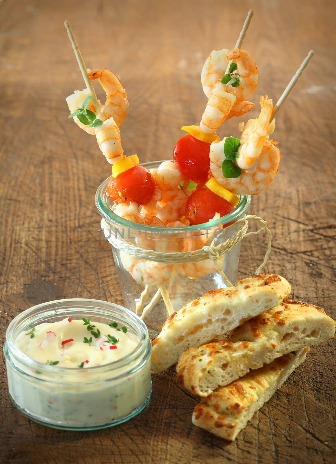 Tasty appetizers of seafood cocktail sticks with shrimps, cheese and tomato standing in a jar alongside fresh focaccia bread and a tub of tartare sauce