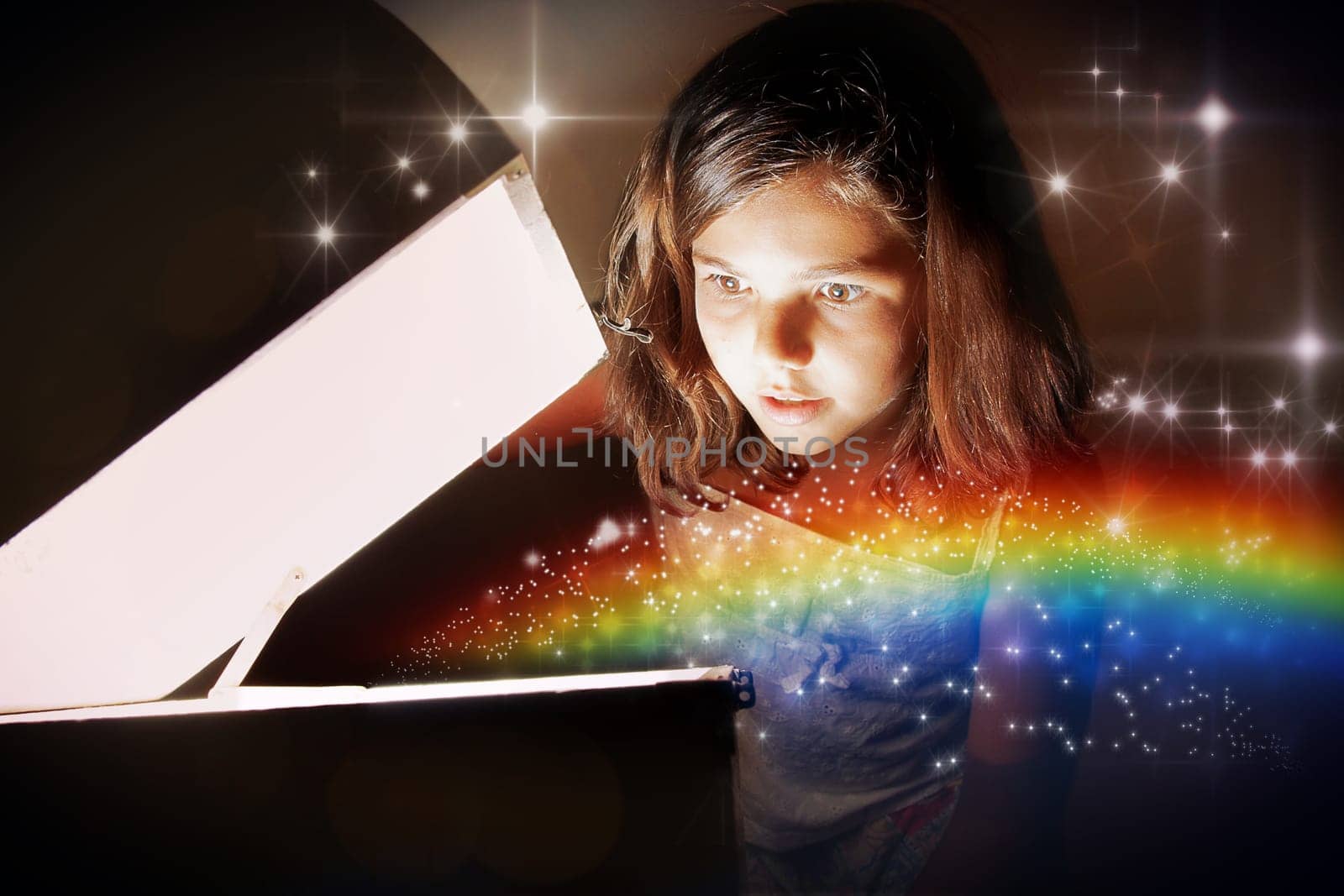 A little girl opening a magic chest and setting the rainbow free amongst glittering stars. Christmas or birthday concept  the magic of gifts.
