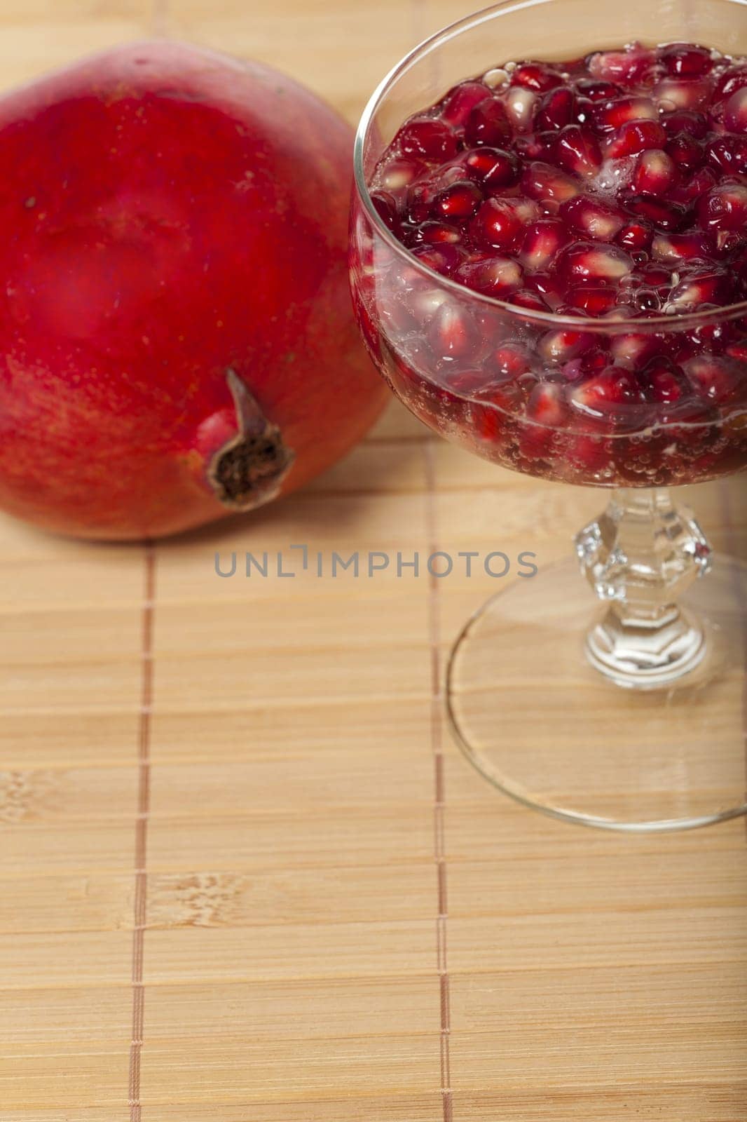 Pomegranate seeds in a champagne glass filled with sparkling wine on a bamboo mat