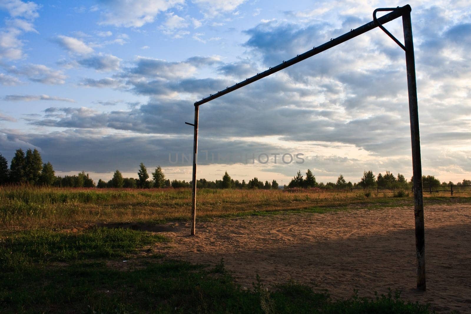 goal without net on old sand field in summer with green field and blue cloudy sky in background