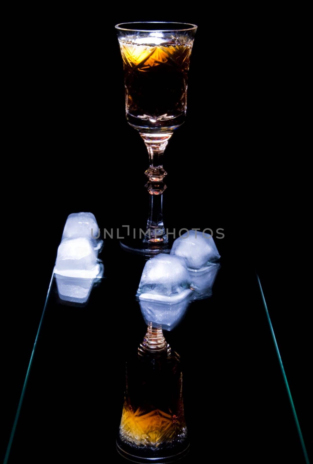 photo of still life with goblet  of alcohol and ice with reflections isolated on dark background