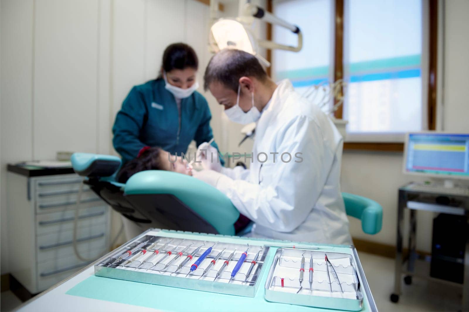Close up of dental equipment in hospital with patient lying on couch and dentist working. Focus on foreground