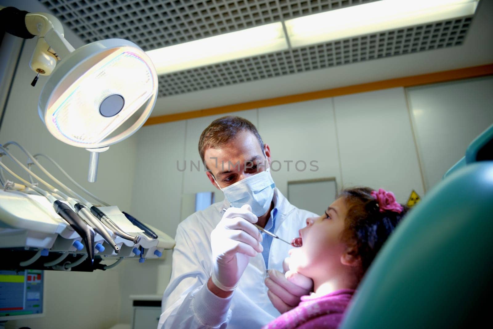 Doctor during visit of female child in dental clinic, dentist checking teeth of young baby girl