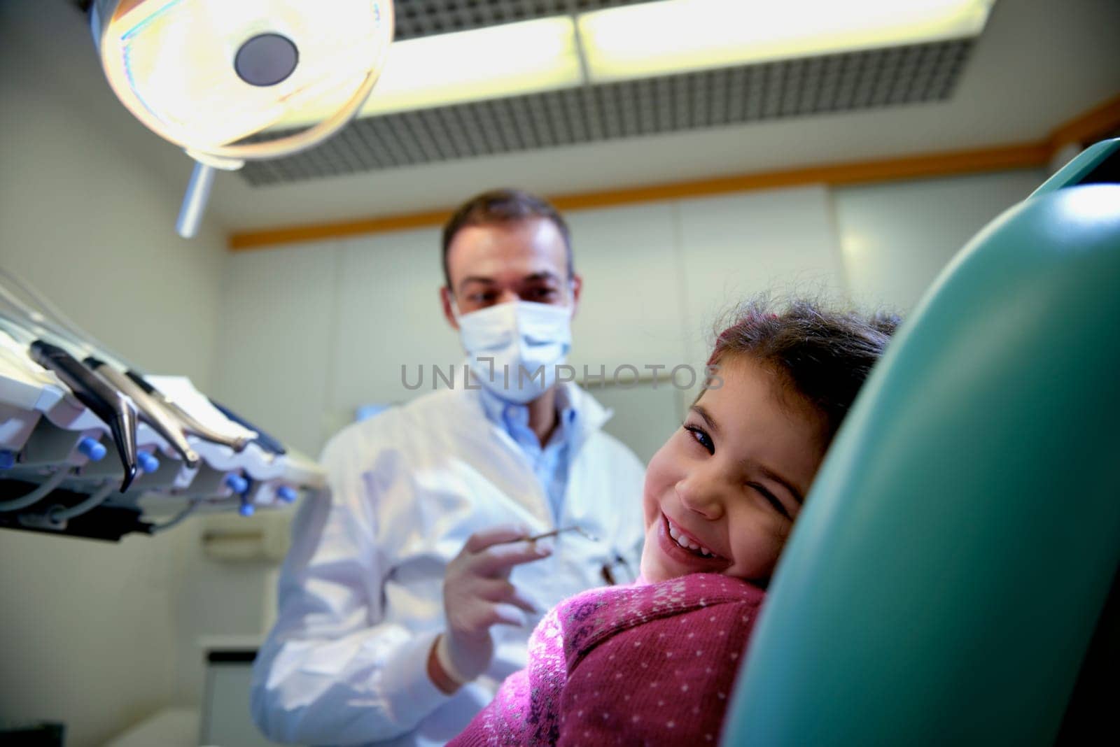 Doctor during visit of female child in dental clinic, portrait of young baby girl looking at camera and smiling