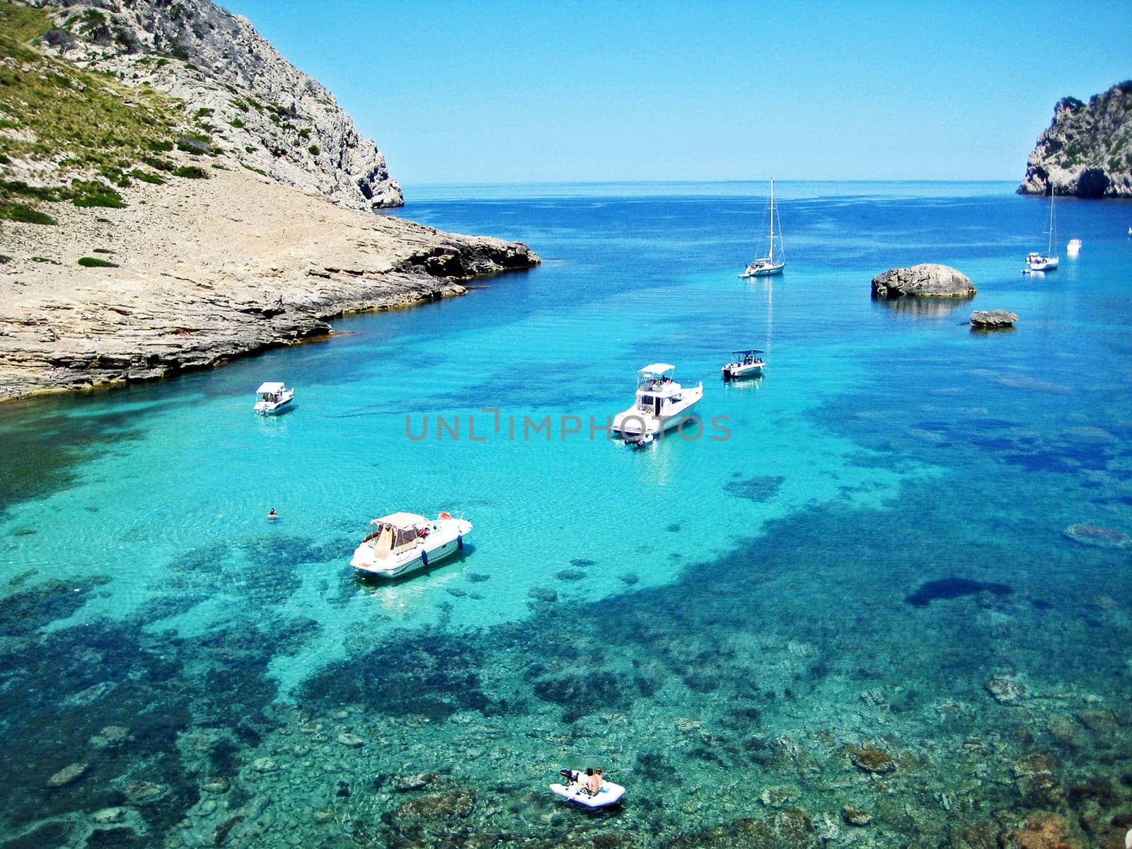 Scenic bay with clear turquoise water, boats, rocks, and mountains