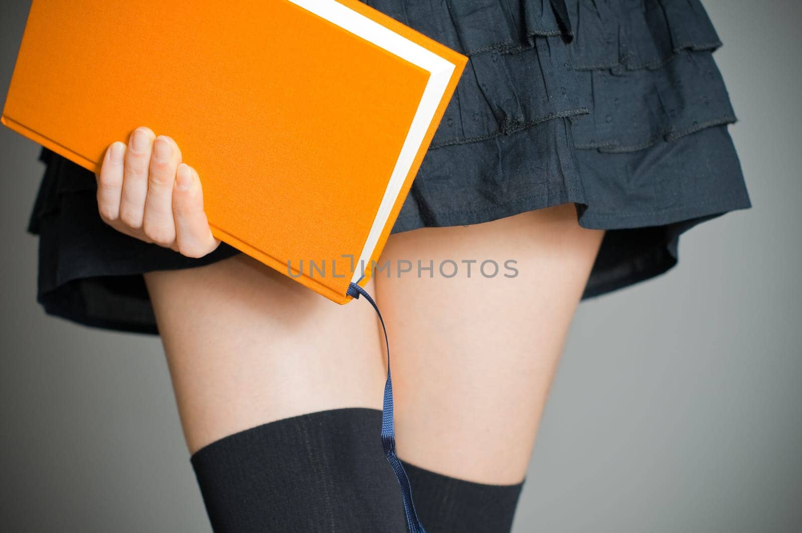 view of the lower body part of woman wearing skirt and stockings holding book in her hands