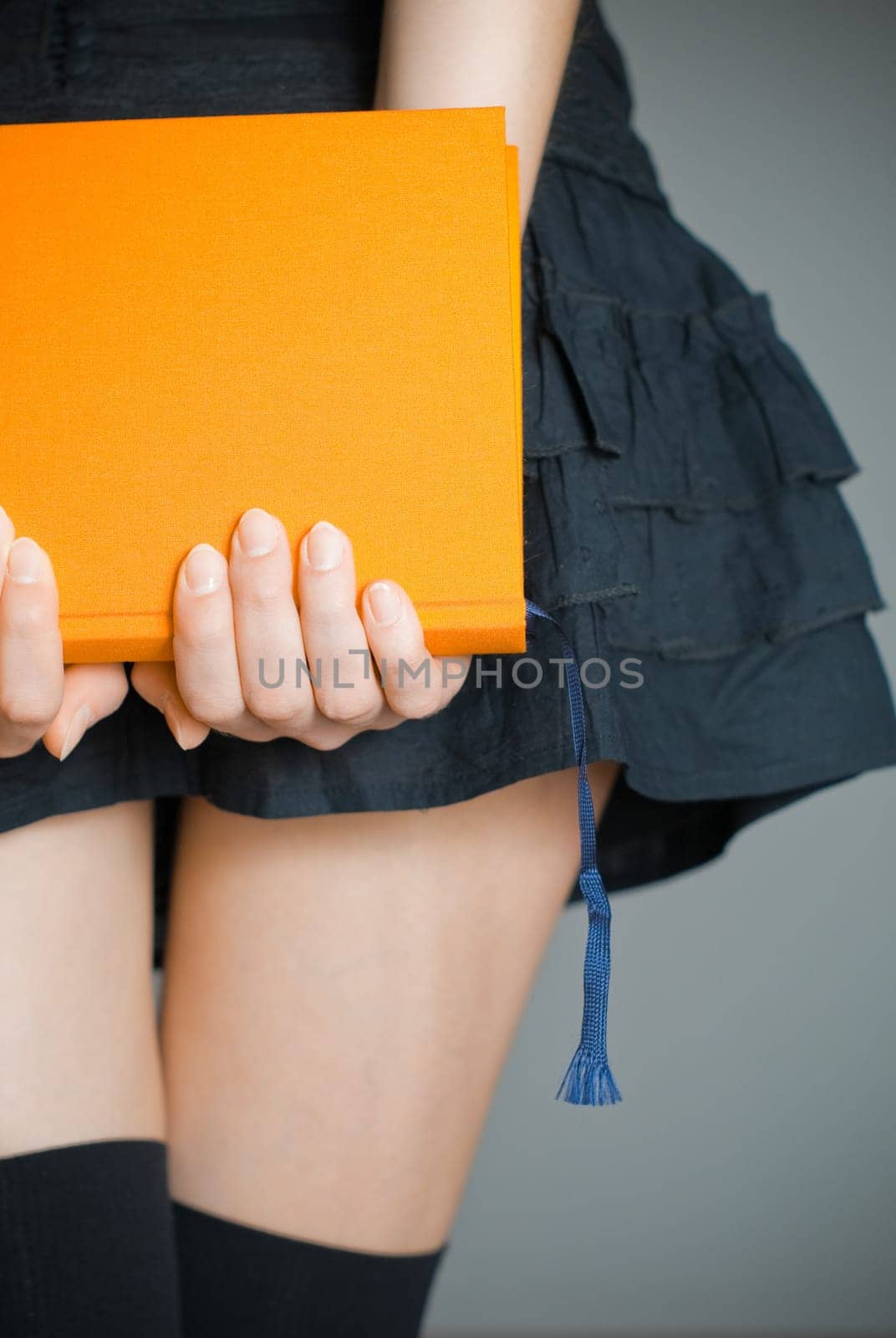 view of the lower body part of woman wearing skirt and stockings holding book in her hands
