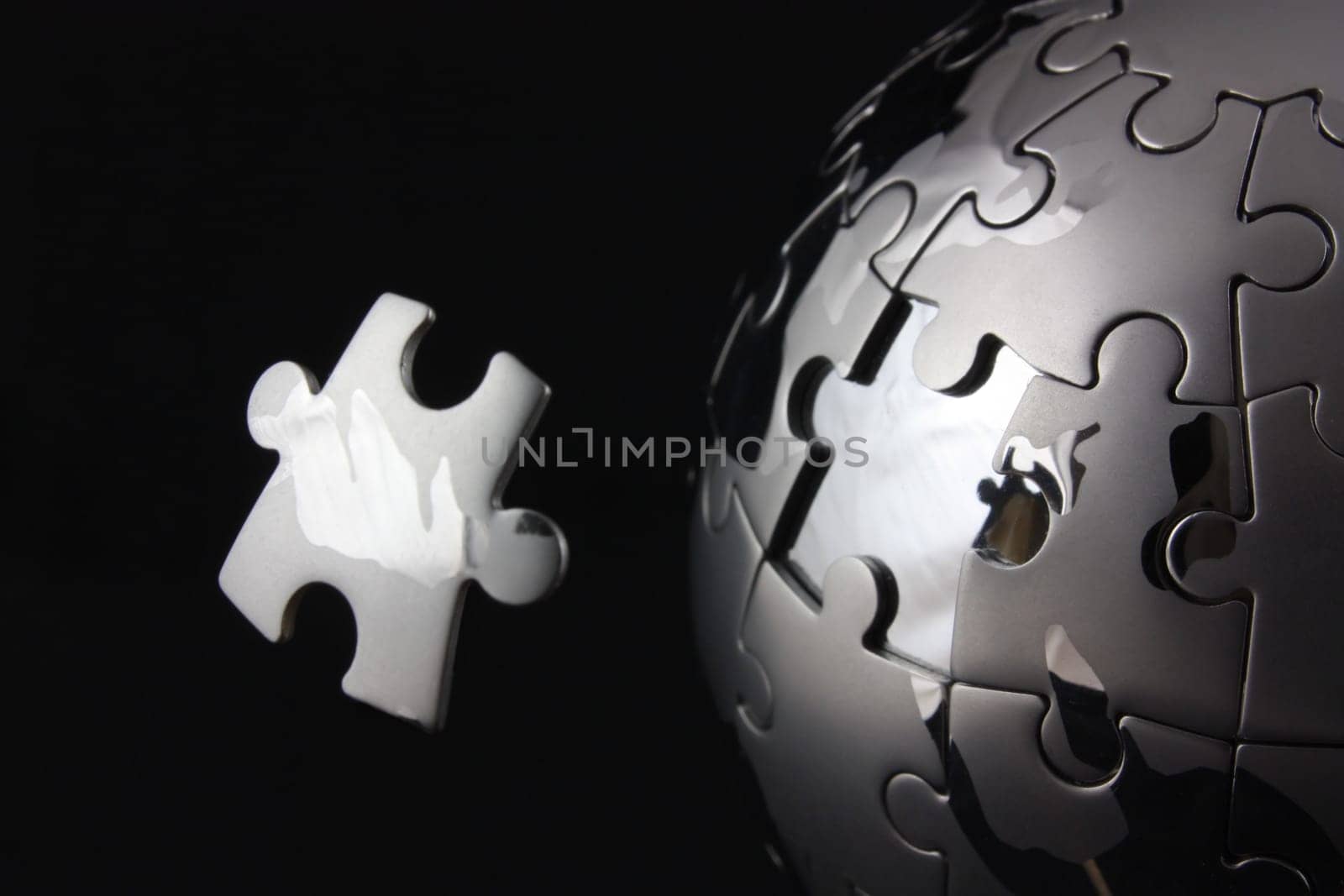 Floating jigsaw peice over chrome puzzle globe