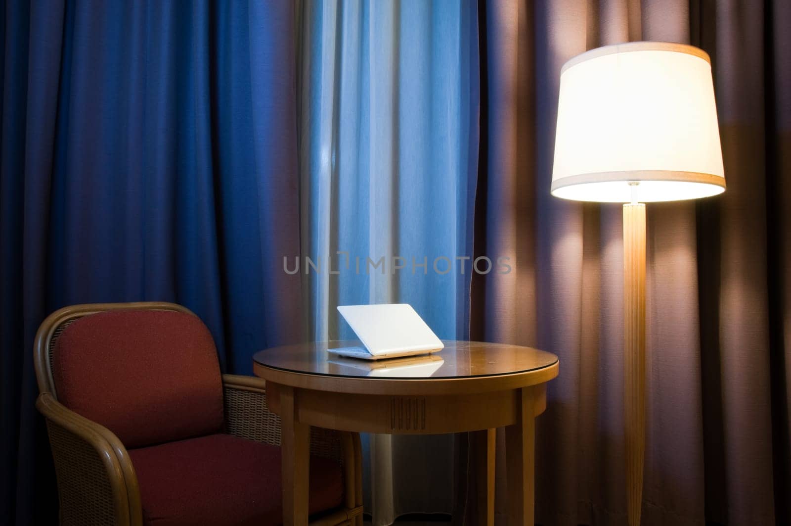 notebook computer on the table in the room with lamp, chair and curtains on the window