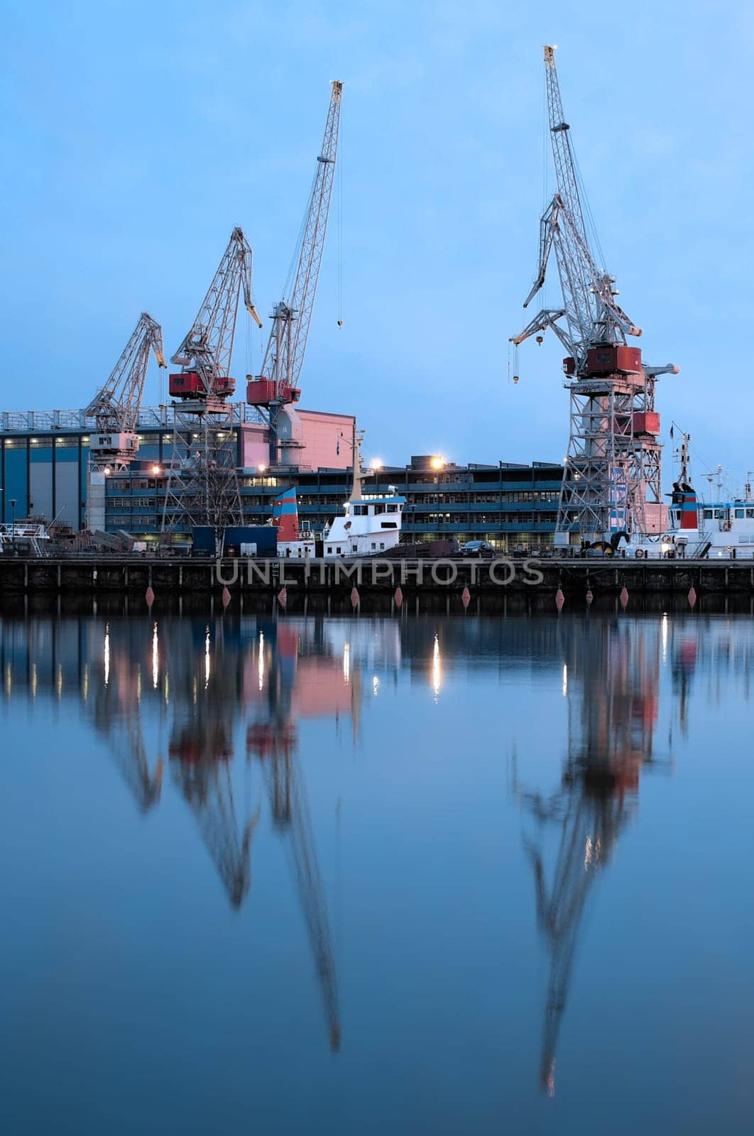 sea port cranes with blue night sky in background and water in foreground in Helsinki port, Finland
