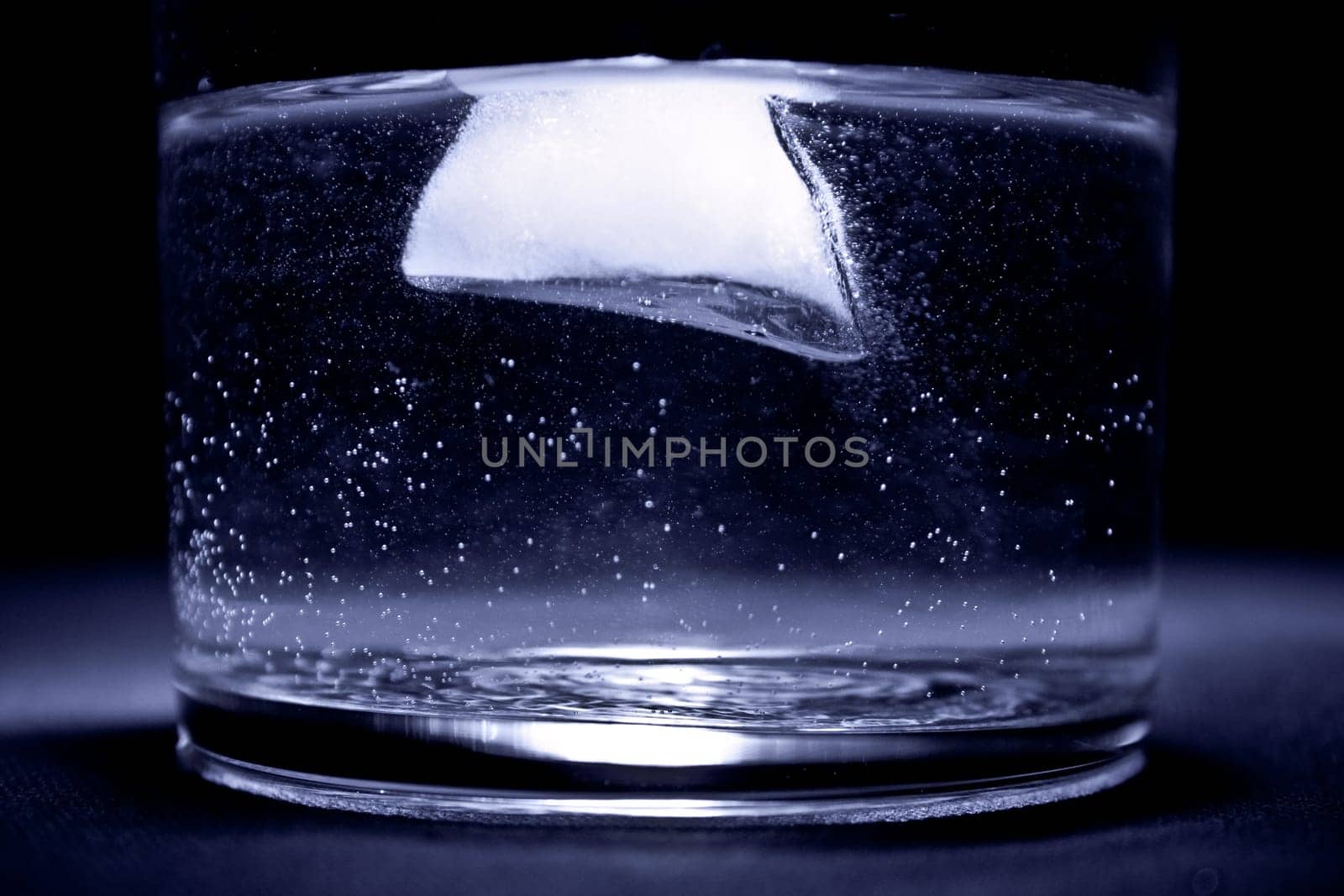 ice floating in the water in the glass with blue tint and black background