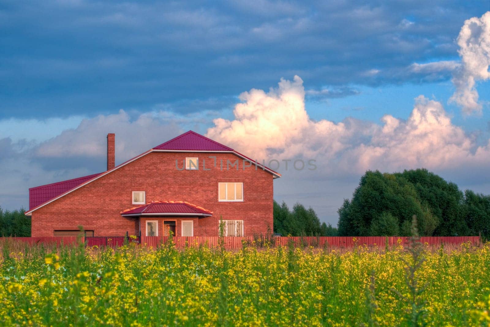red brick house in the field of yellow flowers with cloudy sky in background