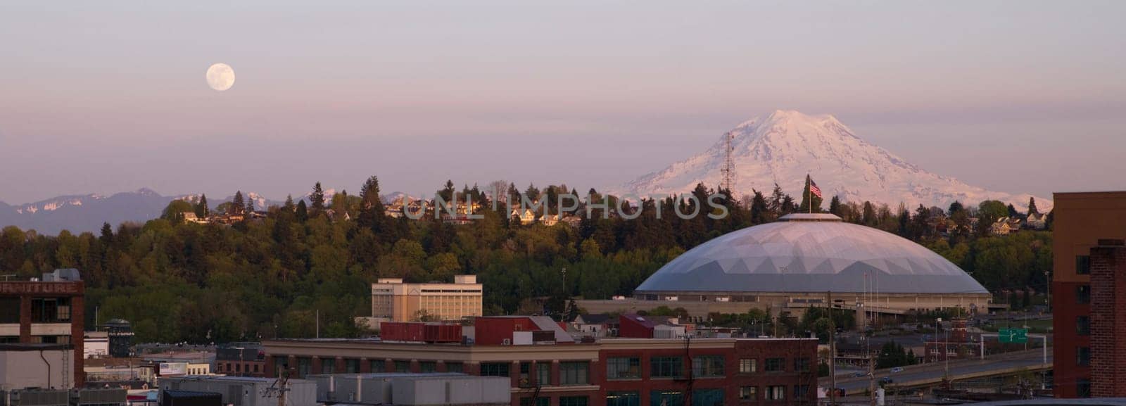 A full moon appears on the horizon near Mt Rainier and the Tacoma Dome