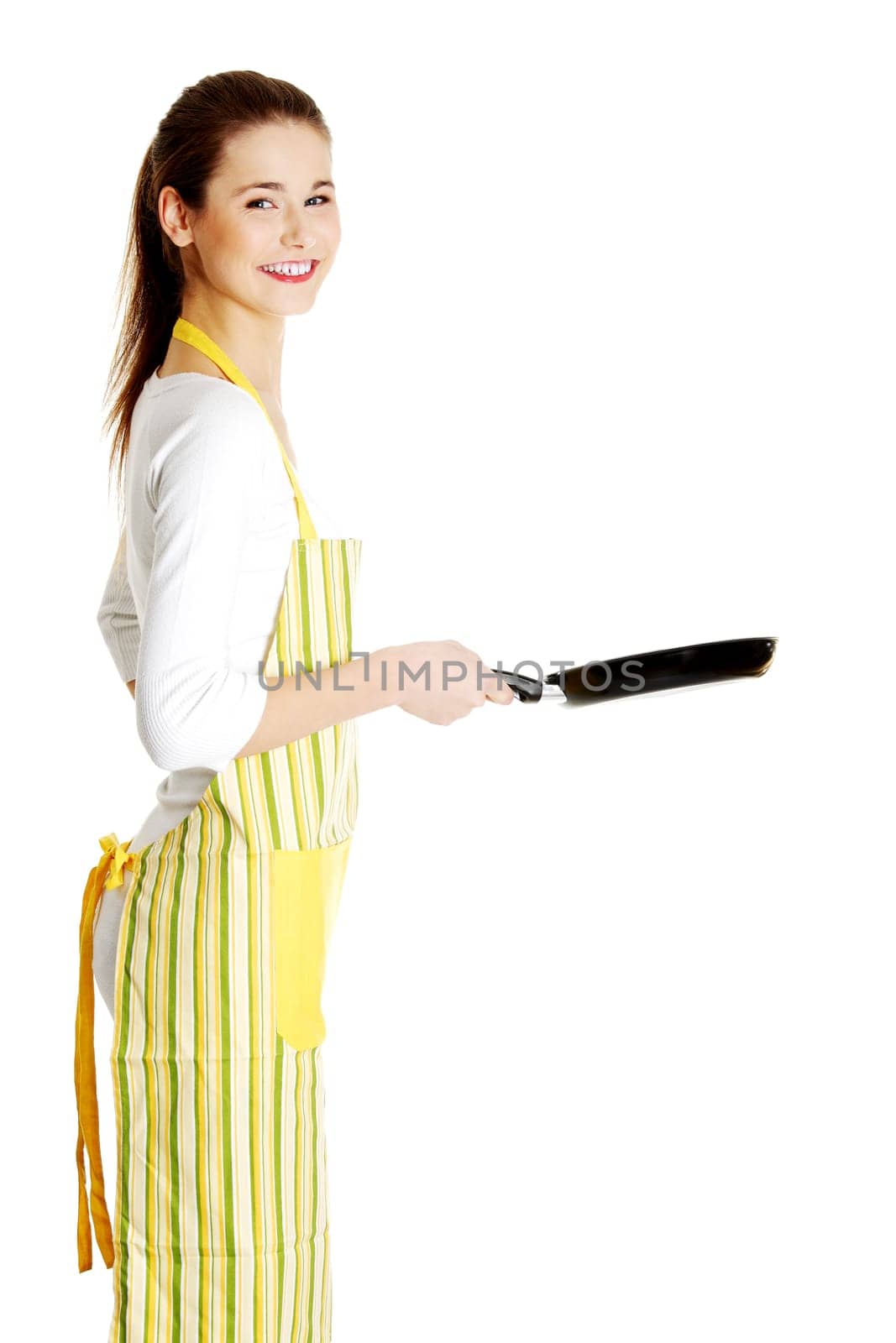 Young smiling caucasian teen girl dressed in apron, smiling behind the frying pan, isolated on white.