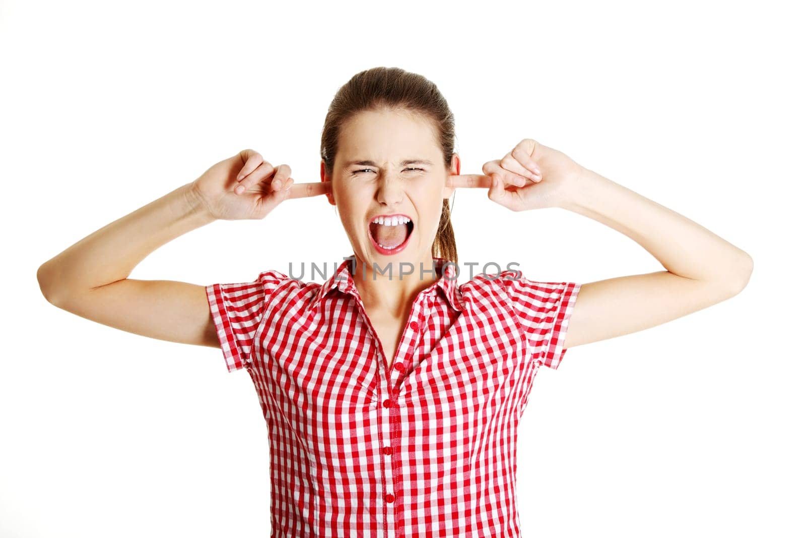 Young angry female caucasian teen clogging her ears and shouting, on white.