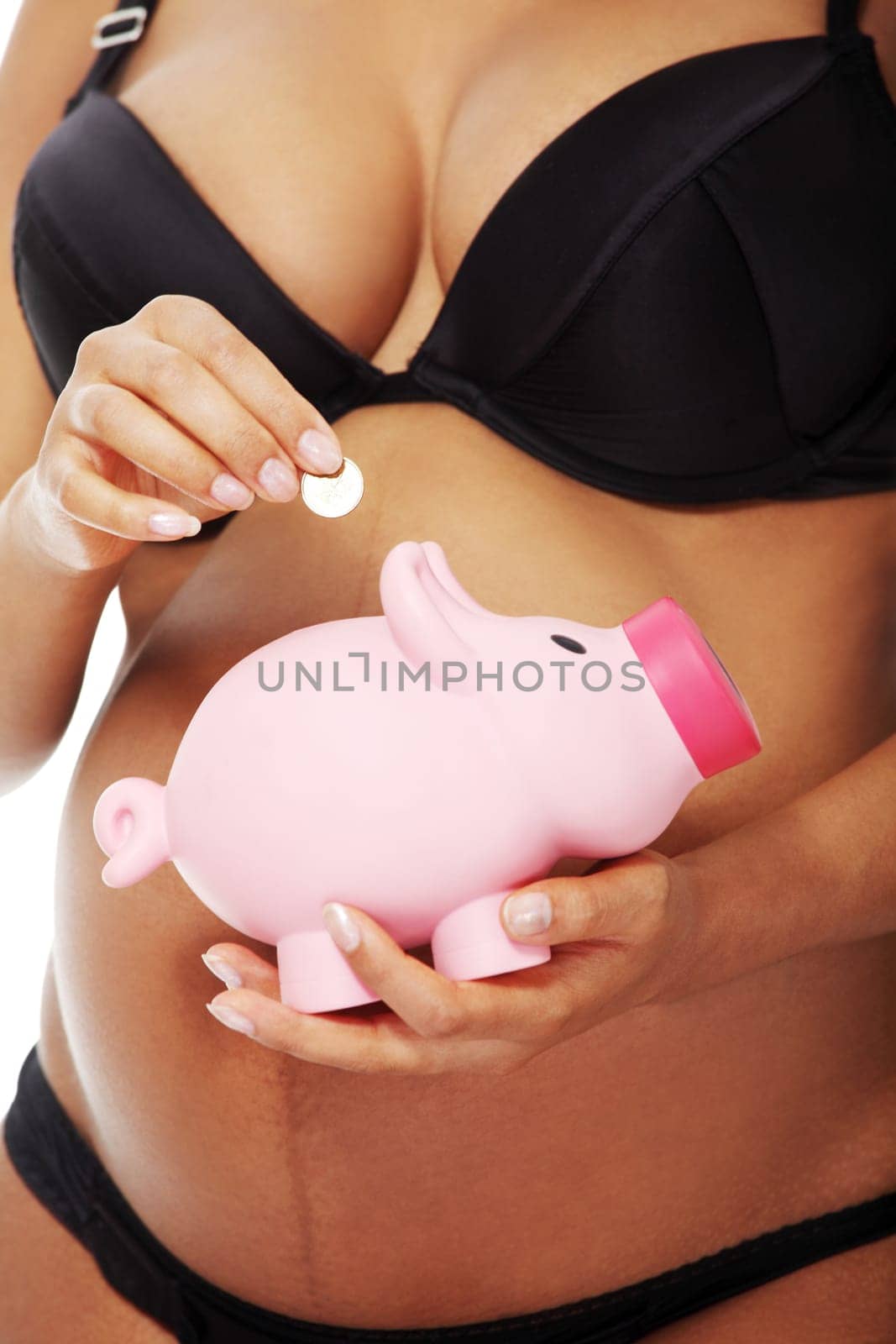 Young beautiful pregnant woman holding a pink piggybank in front of her belly, over a white background.