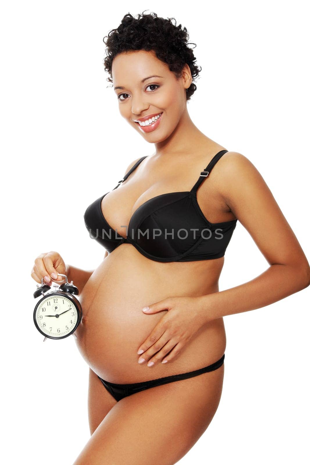 Portrait of a young beautiful pregnant woman holding an alarm clock next to her belly, isolated on a white background.