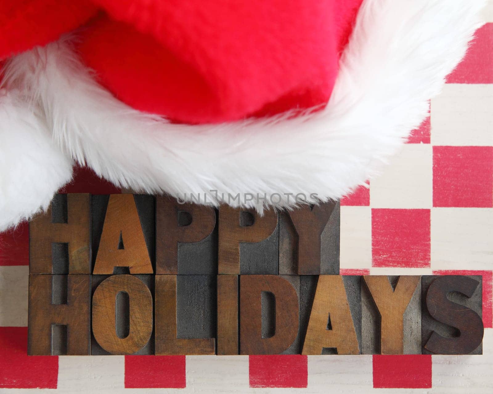 happy holidays in old wood type on a checkerboard with a furry Santa hat