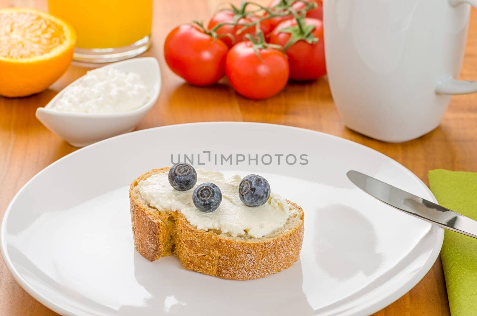 Baguette with cream cheese and blueberries on a set breakfast table
