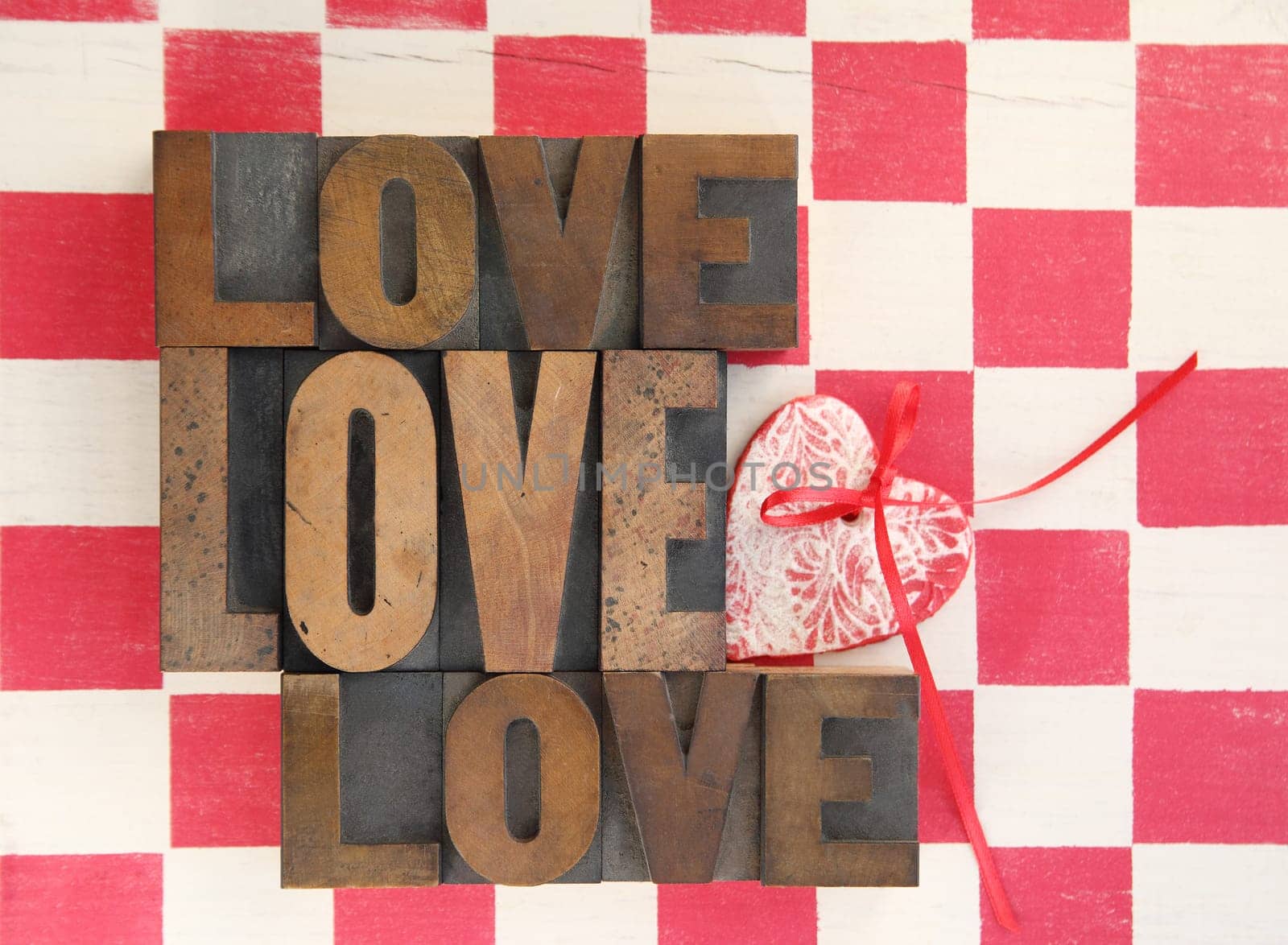 the word love repeated three times with a handmade heart ornament on a checkerboard